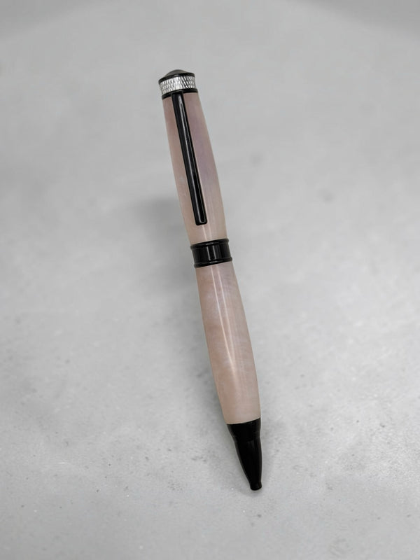Anderson Woodworks handcrafted ballpoint pen with a translucent blush marbled barrel and matte black hardware.