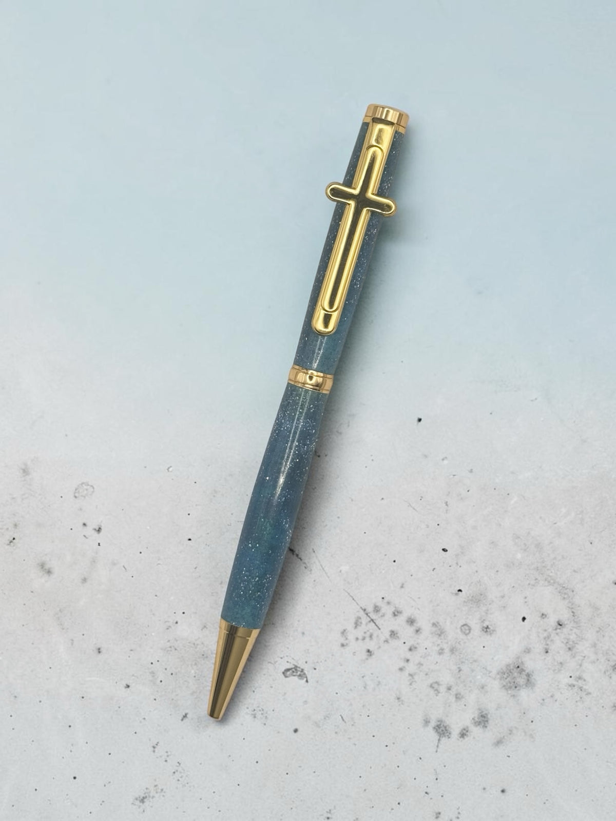 Anderson Woodworks handcrafted ballpoint pen with a blue shimmering resin barrel and gold cross clip.