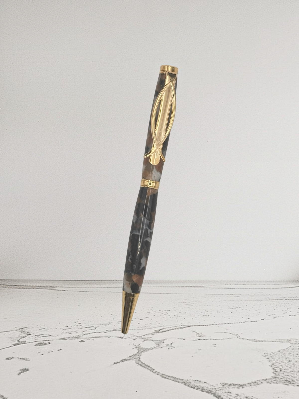 Anderson Woodworks handcrafted ballpoint pen with a marbled charcoal, cream, and brown resin barrel and gold hardware.