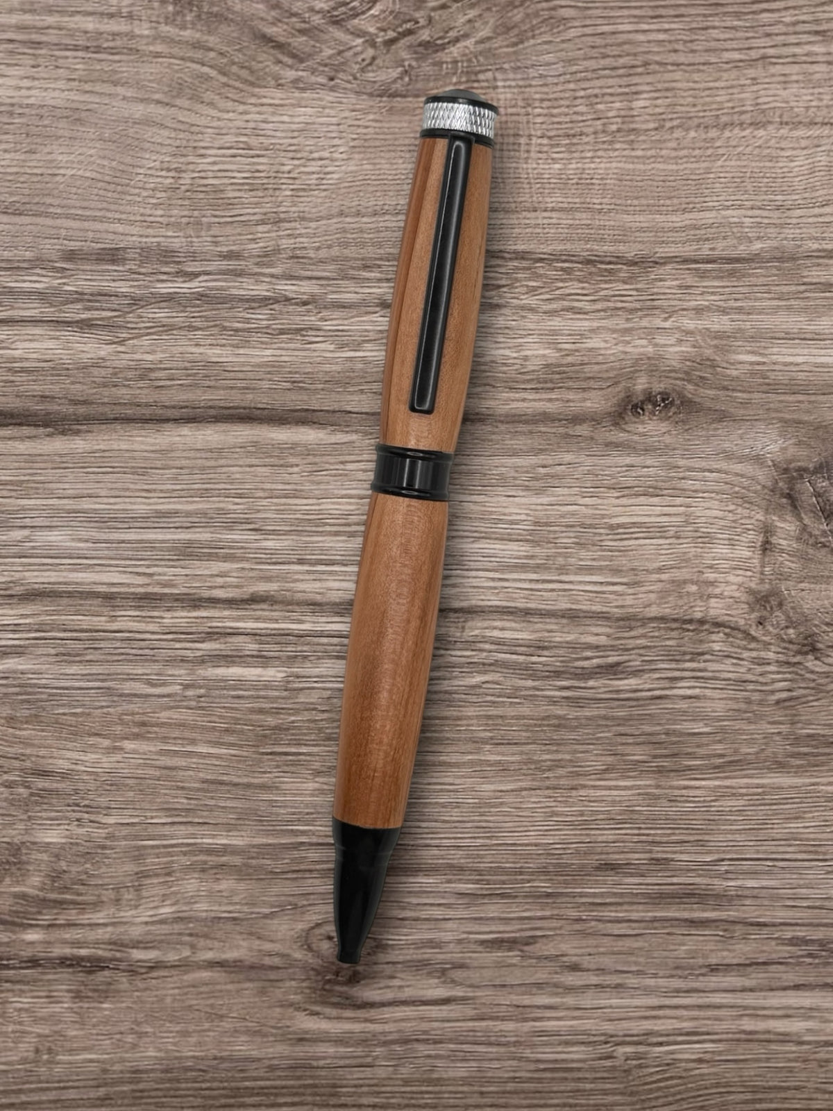 Anderson Woodworks handcrafted wooden ballpoint pen with matte black hardware and silver knurled cap on wood surface